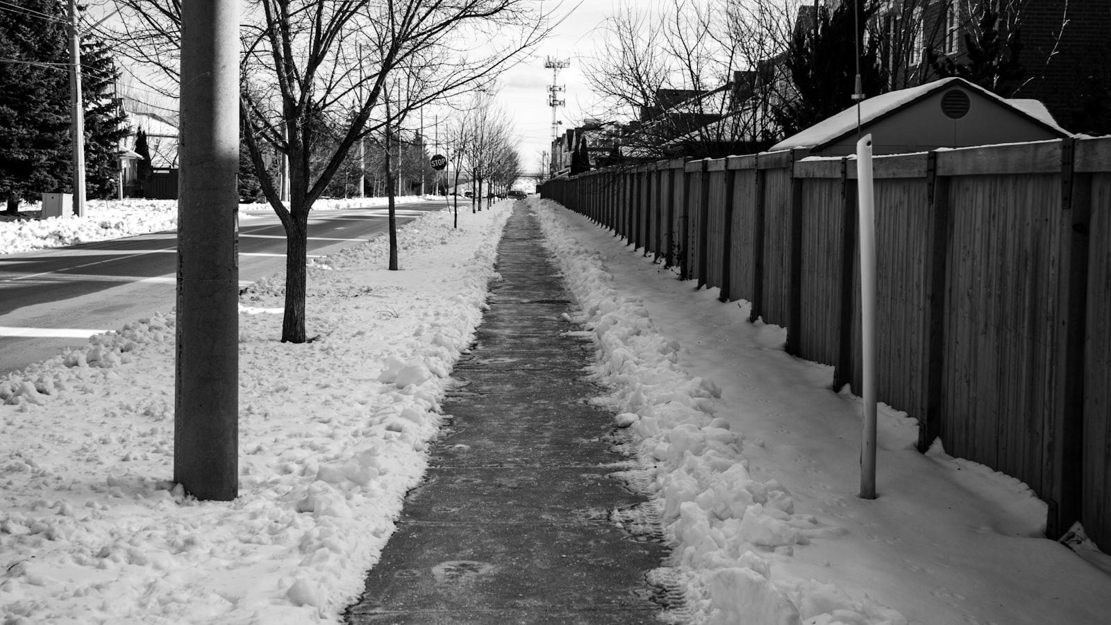 A snow covered sidewalk running beside a wooden fence